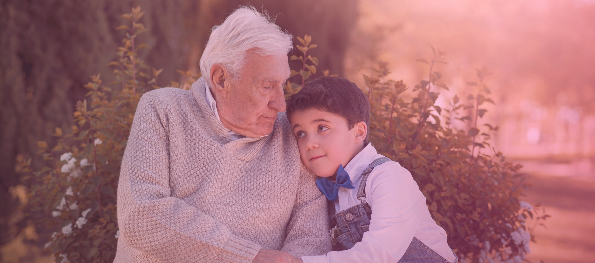 Tender moment between gifts for a grandfather and grandson in a serene outdoor setting, showcasing a close bond and loving interaction, with soft sunlight filtering through the background.